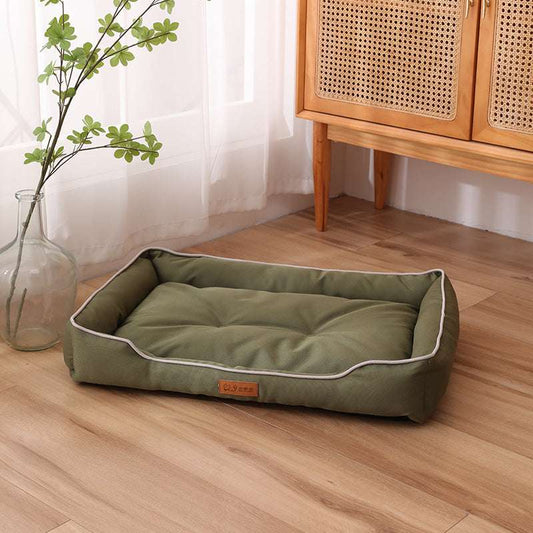 Green pet bed on a wooden floor with a wooden cabinet and plant in the background