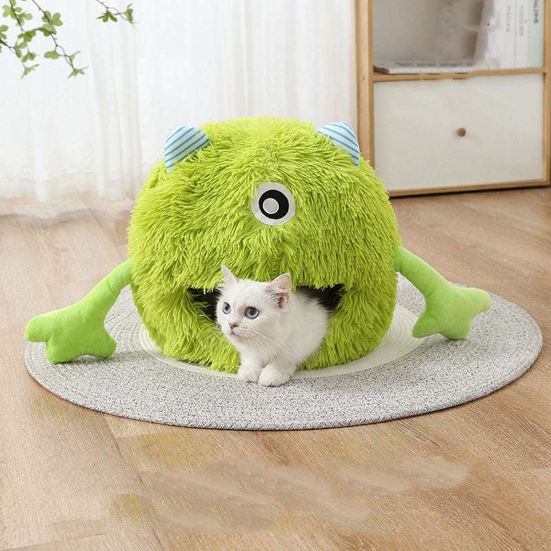 Green plush monster-shaped pet bed with a cat inside on a wooden floor.