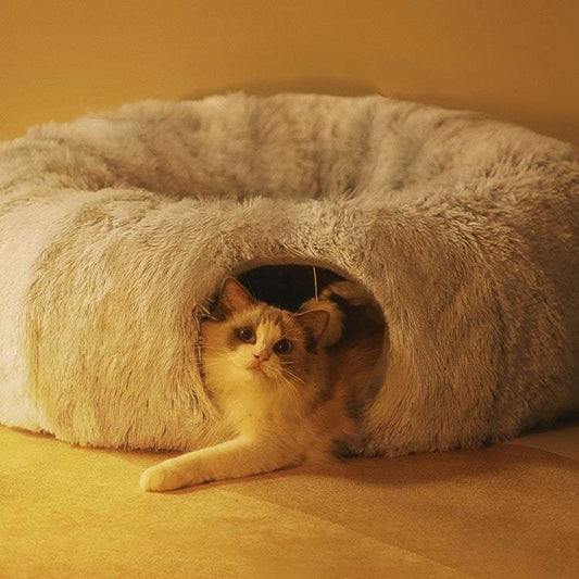 Cat peeking out from a fluffy gray pet bed on a warm-toned floor.