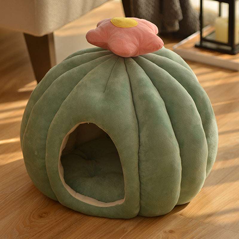Green pet bed shaped like a cactus with a pink flower on top, placed on a wooden floor.