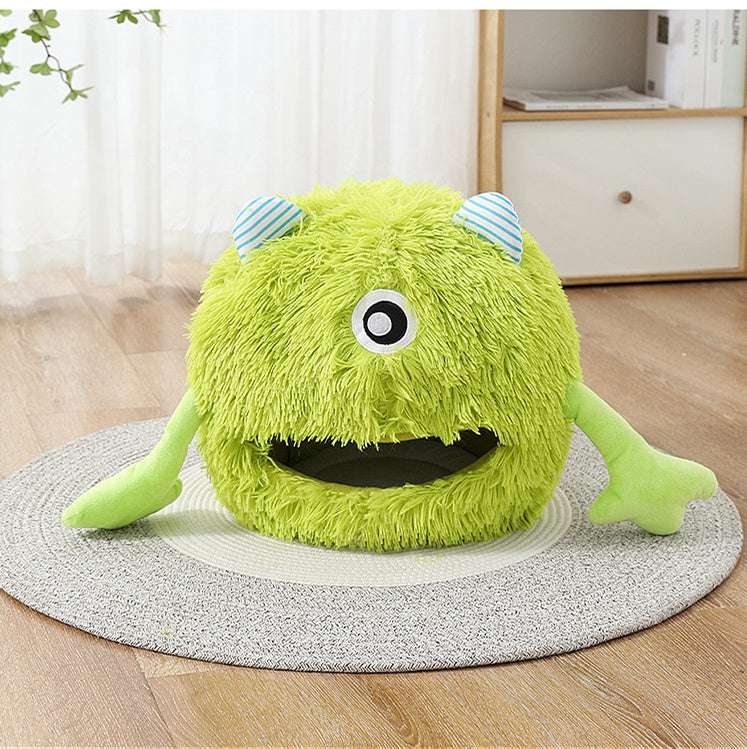 Green plush toy with one eye and striped blue ears on a round mat.
