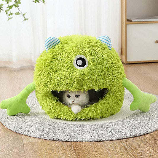 Green monster-shaped pet bed with a cat peeking out on a wooden floor.