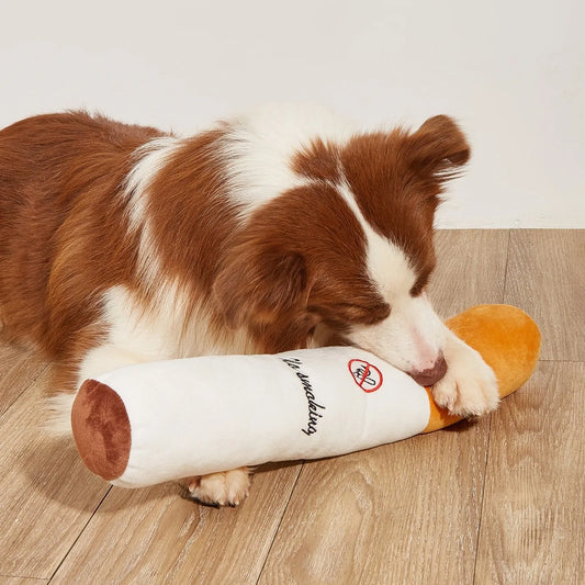 Dog playing with a plush toy resembling a bone on a wooden floor.